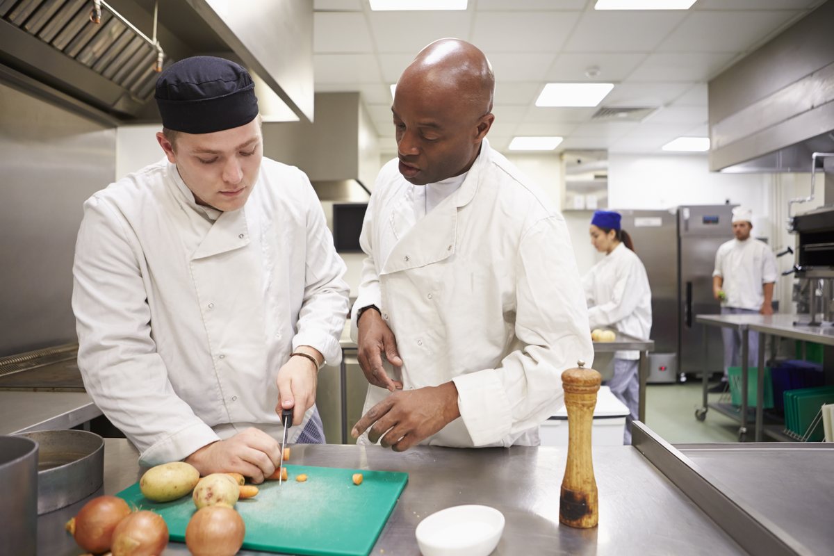A tutor helping catering students in a training kitchen